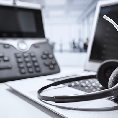 Headset next to a laptop and phone on a desk in a professional setting.